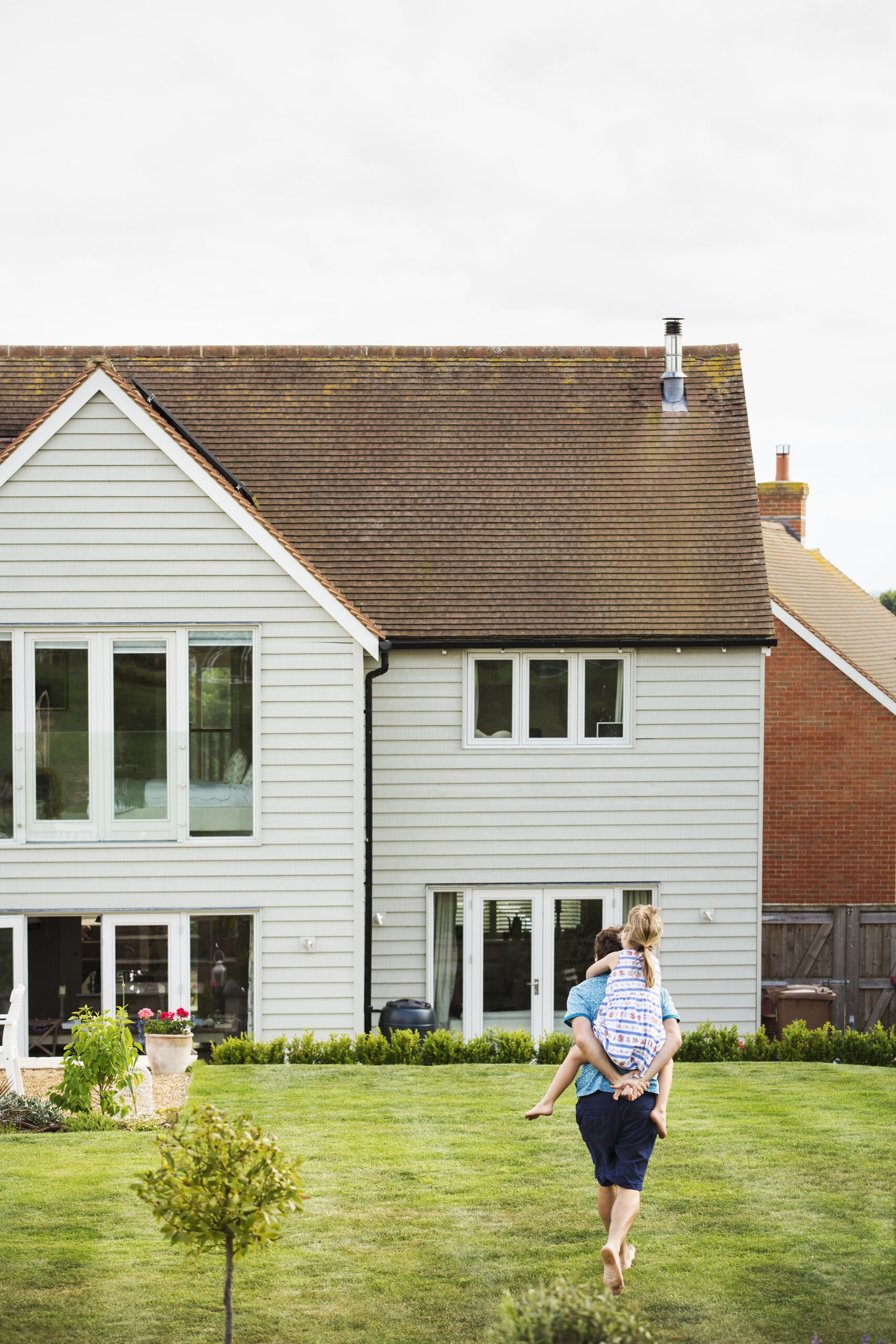 Rear view of a man walking across a lawn, giving a piggyback to a young girl.